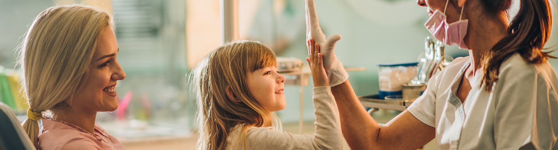 smiling mother holding her little girl as she high-fives her dentist