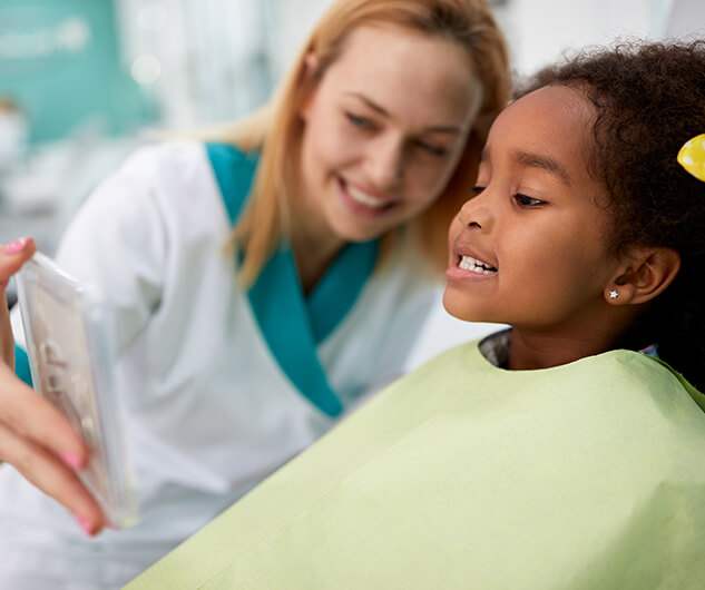 young girl looking at her teeth in a phone at the dentist