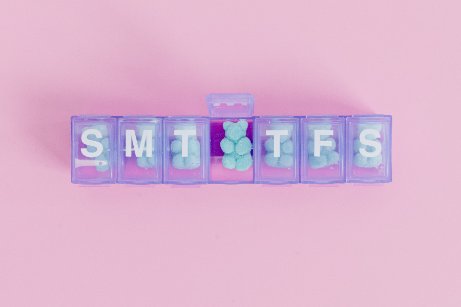 Blue gummy vitamins in a purple pill organizer for kids on a pink background