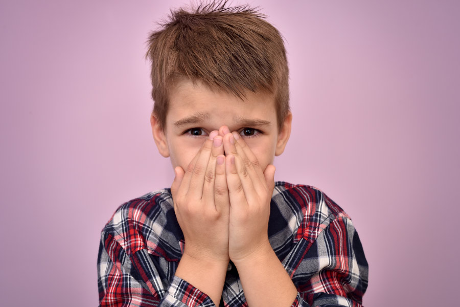 Boy with light brown hair in a plaid shirt covers his mouth because of bad breath in Columbus, OH
